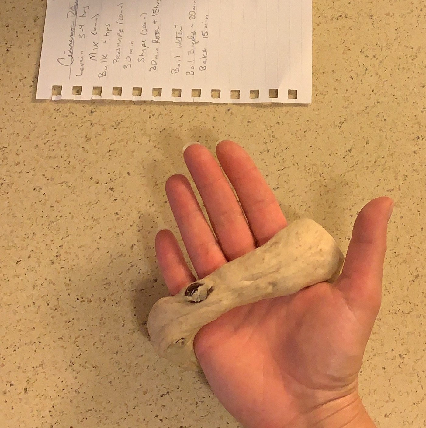 hand with bagel dough wrapped around the palm, next to a piece of notebook paper on the counter