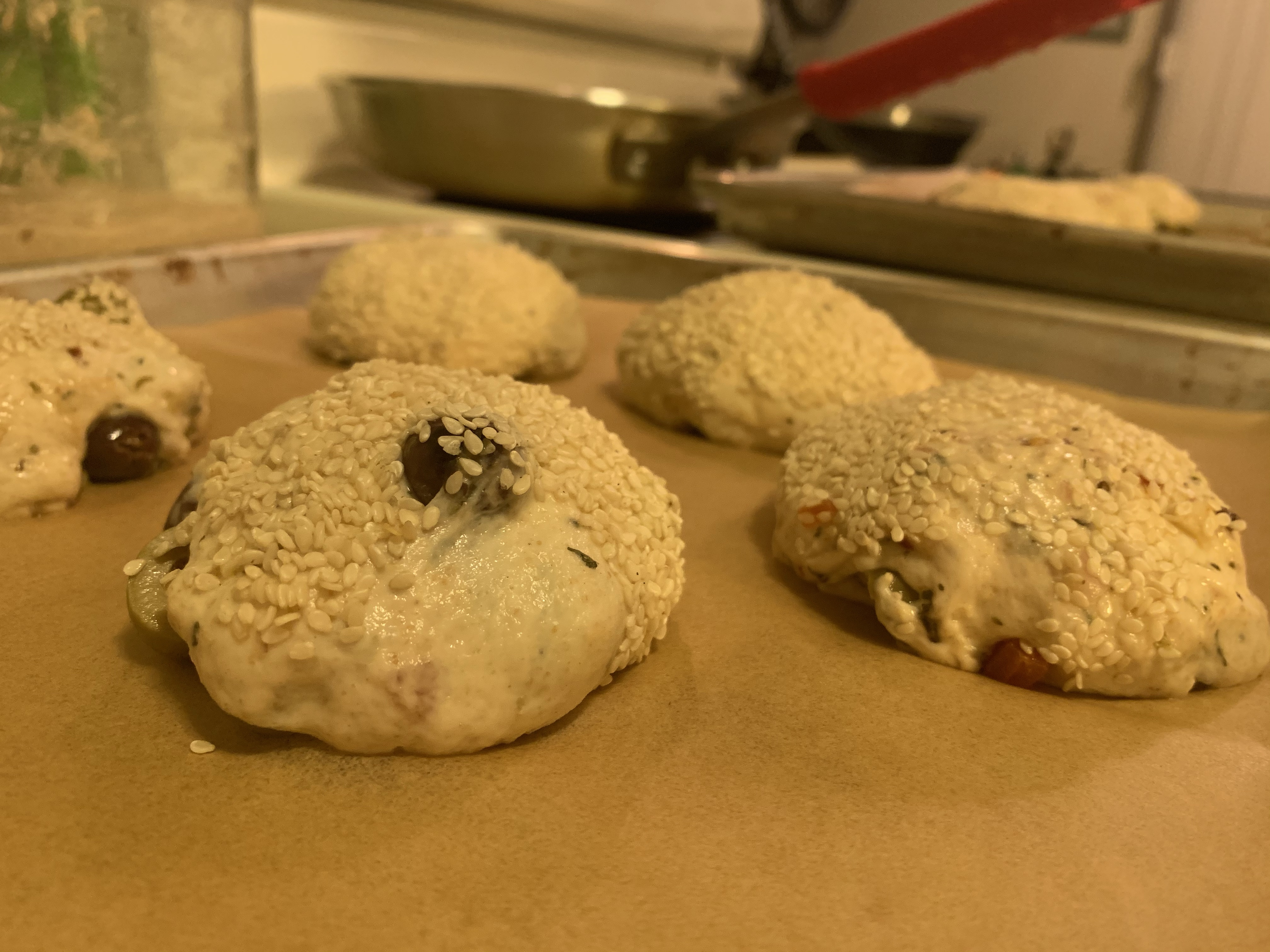 Close up of shaped rolls, covered in sesame seeds, on parchment paper.