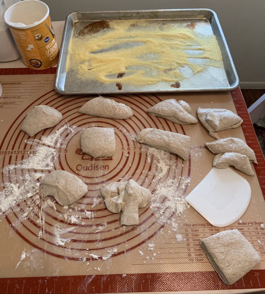 Rubber mat with ten piles or cuts of dough. Above is a baking sheet covered in cornmeal next to a cannister of cornmeal.