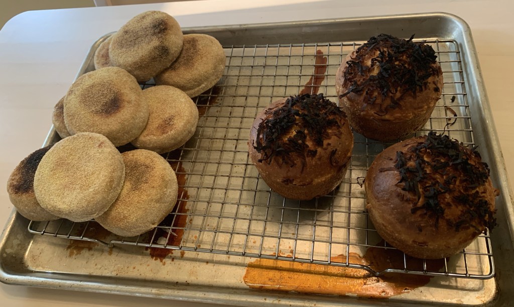 Cooling rack with nine English muffins on the left and three pan de coco buns on the right.