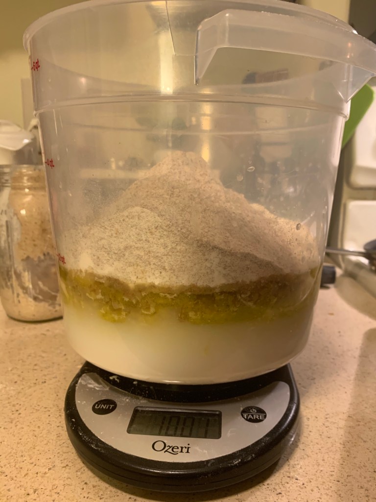 6qt clear container on a kitchen scale. In the container you can see layers of ingredients, with murky water on the bottom, an oily dark middle layer, and topped with flour.