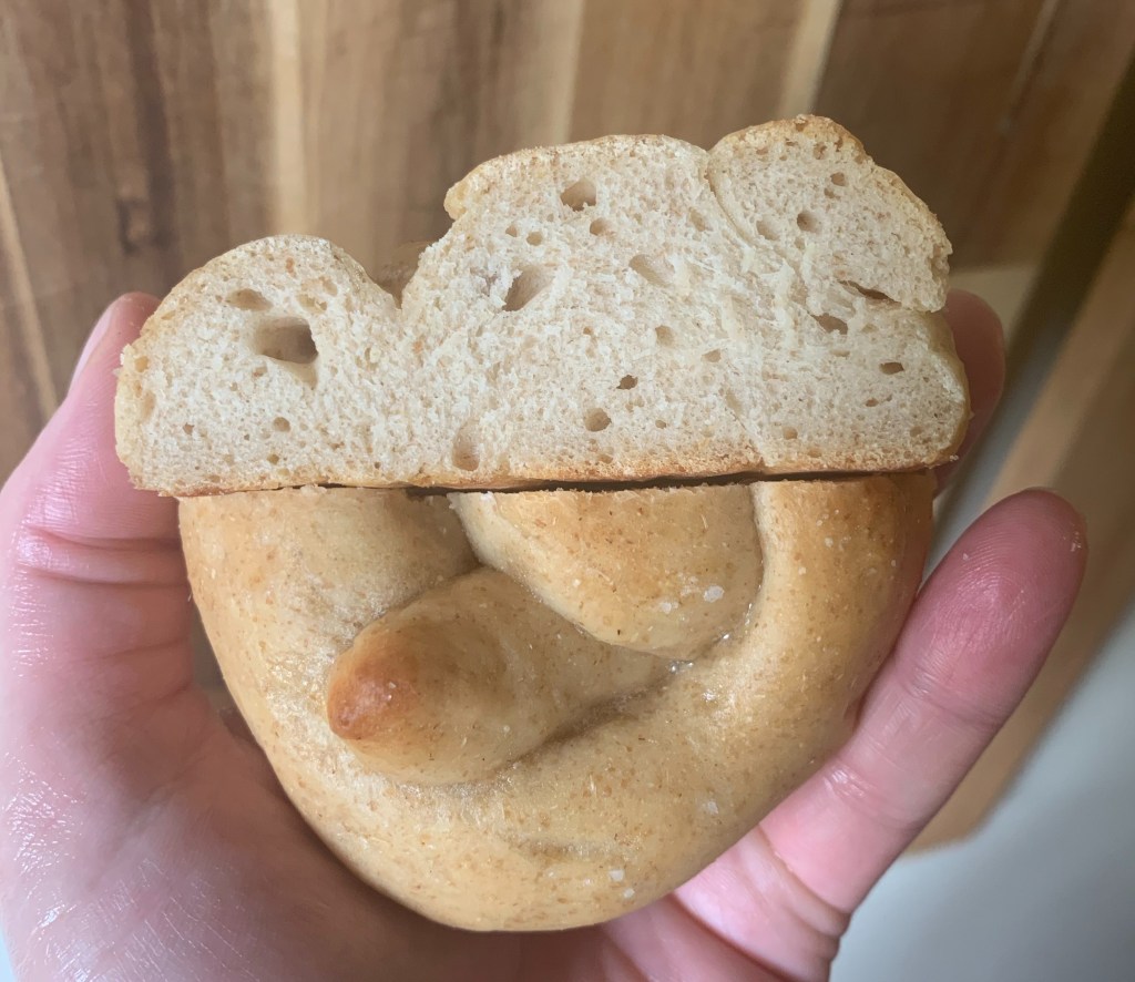 Hand holding two halves of small, light brown pretzel. Bottom half shows top of pretzel crust. Top half shows inner crumb with small air pockets.