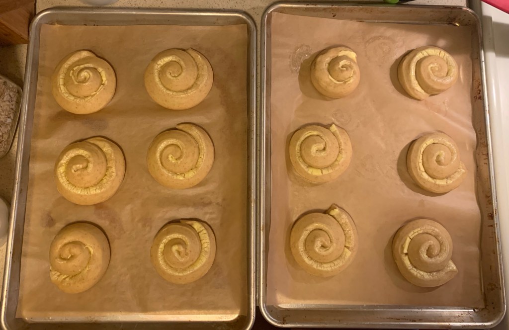 Two trays of six mallorca coils each, after proofing. They had spread out, and the strips of butter and sugar are yellow and crackled.