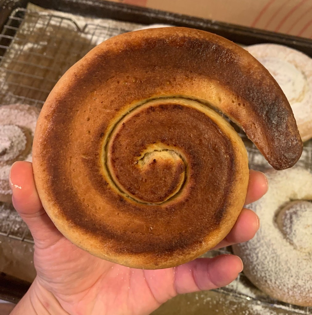 Hand holding mallorca, showing bottom of bun. It is flat and dark.