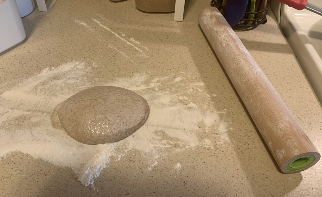 round of dough on a floured counter next to a rolling pin