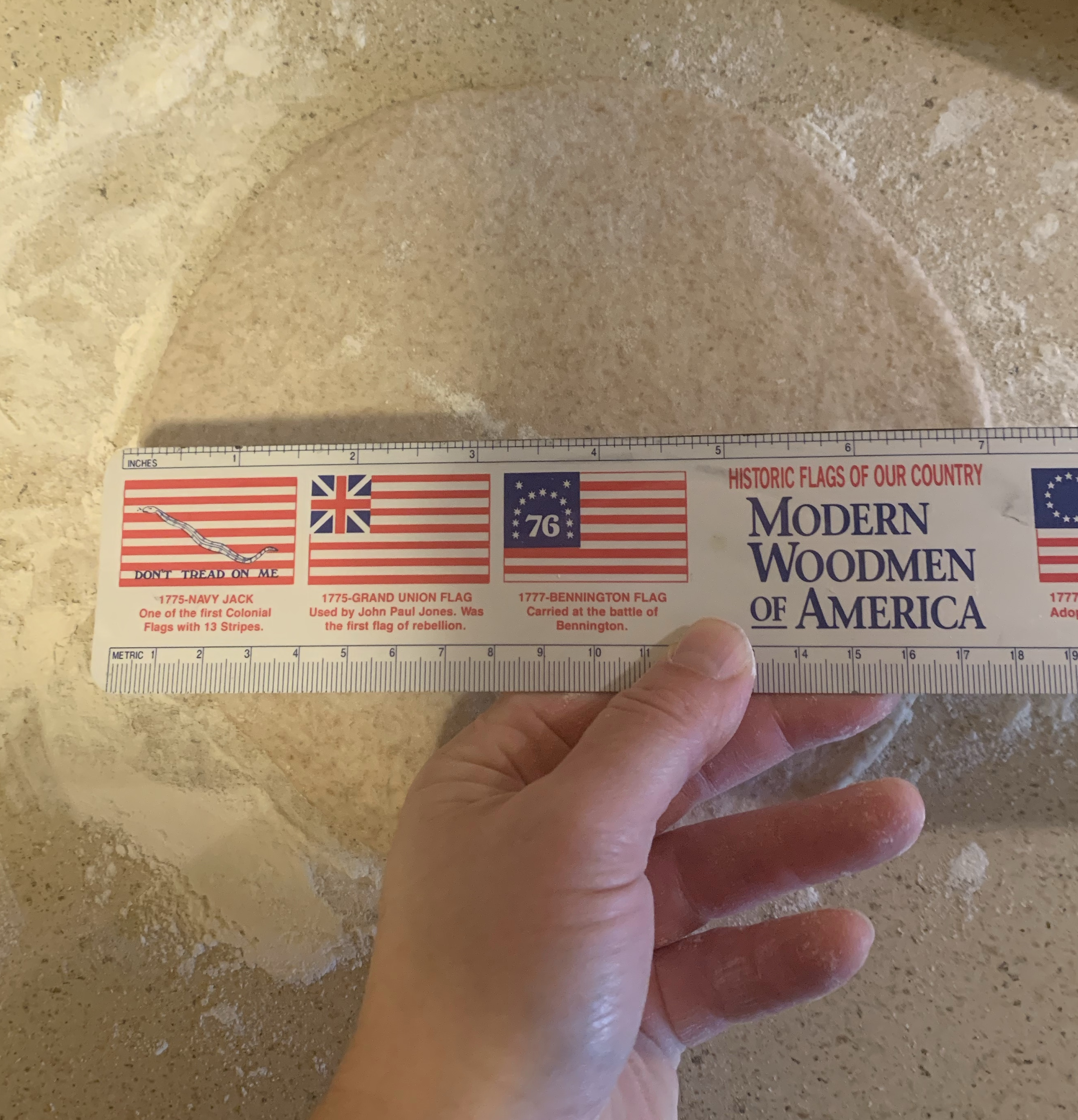 hand holding ruler over rolled out round of dough next to rolling pin