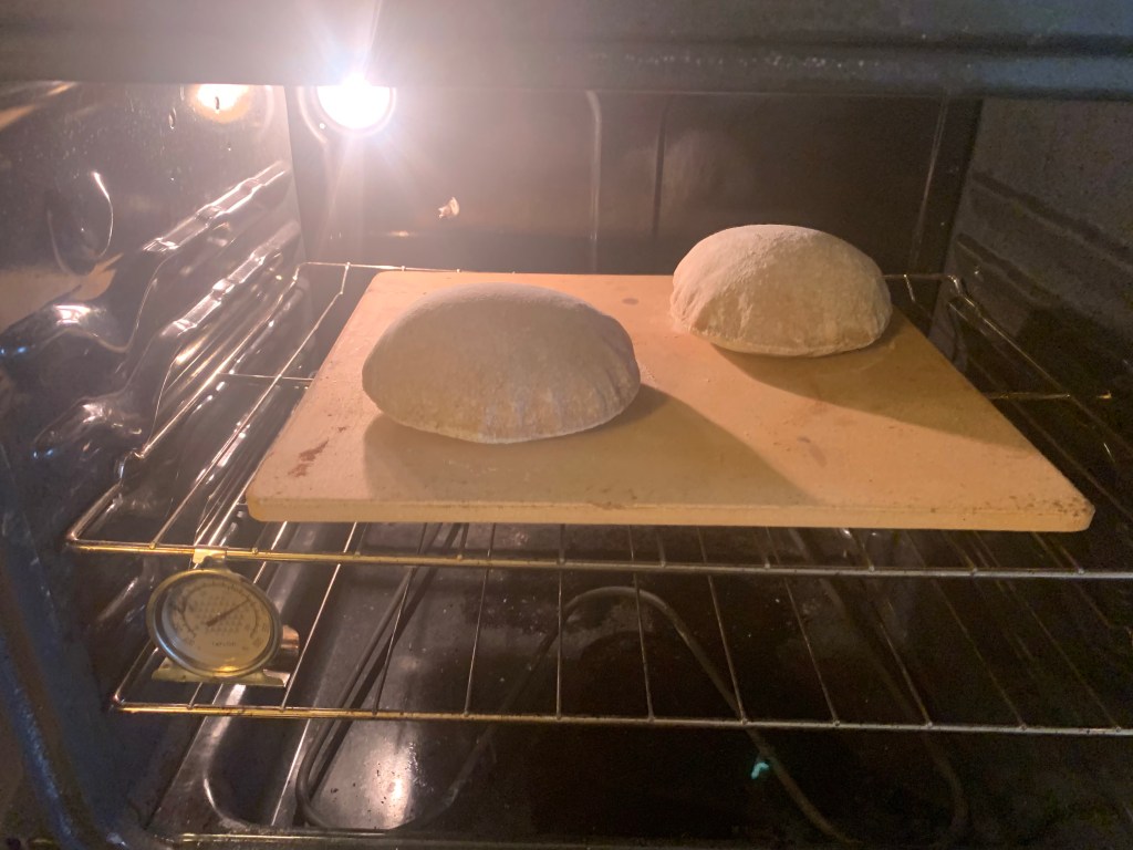 two ballooned pitas on a baking stone in an oven.