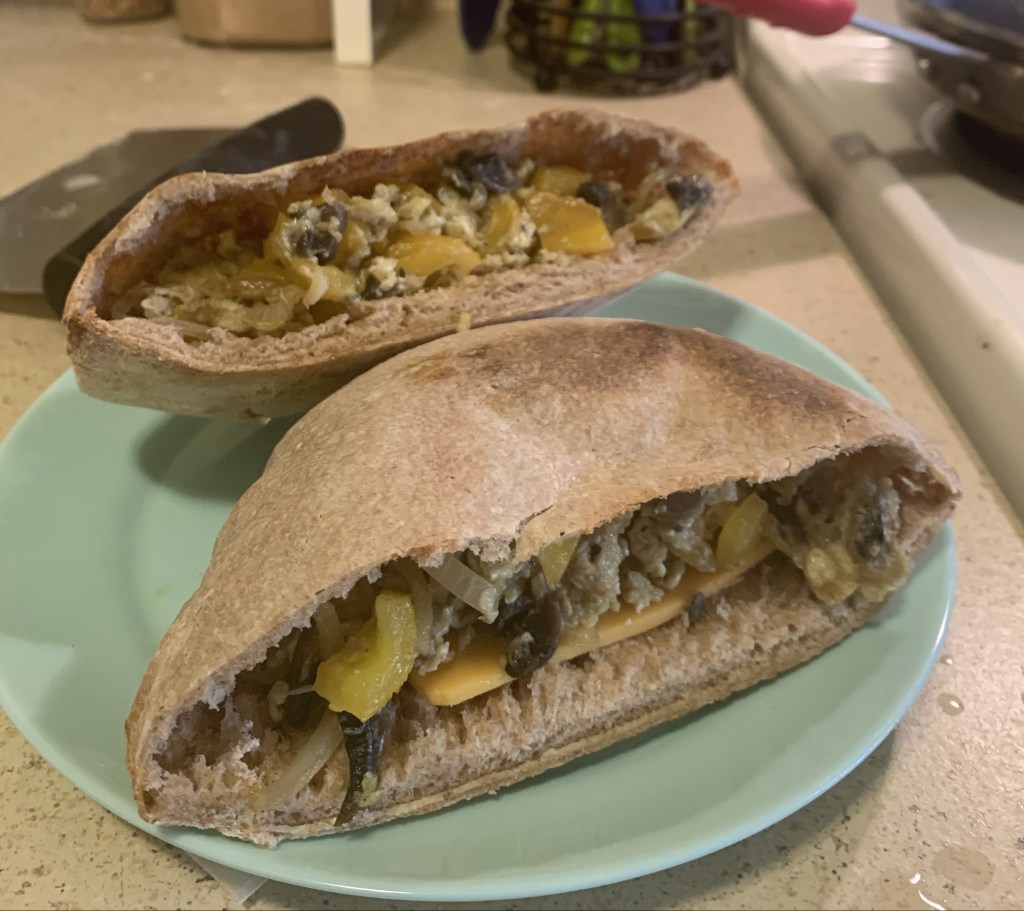 Teal plate with two halves of a pita sandwich with eggs and vegetables