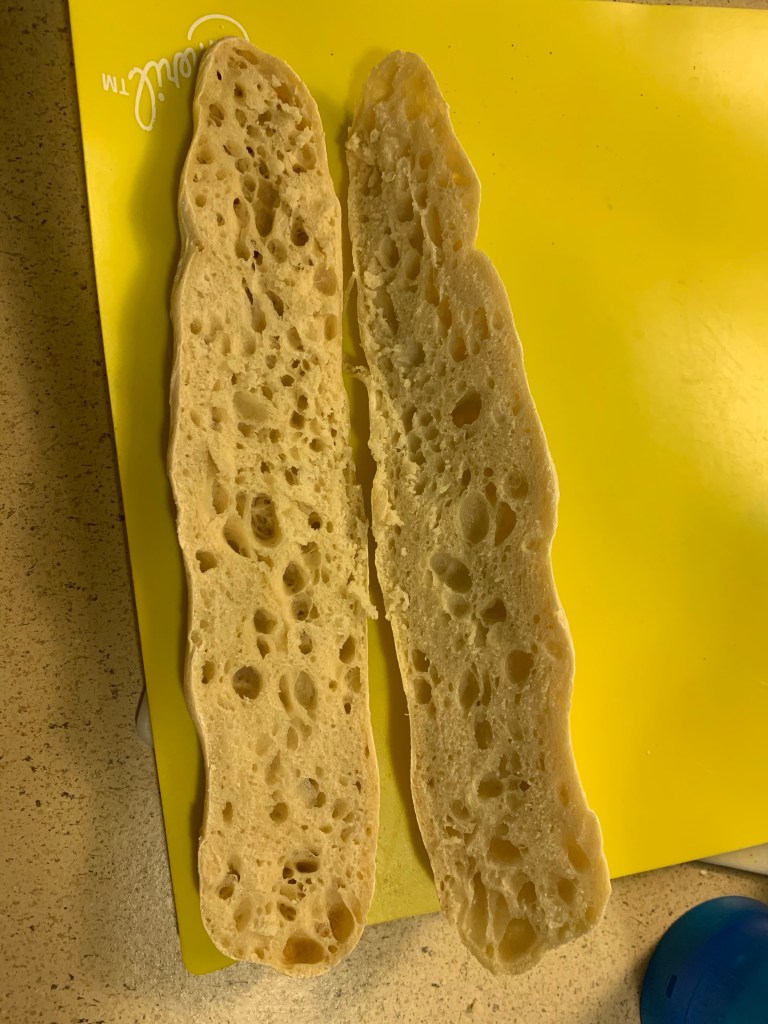 Underbaked demibaguette, cut open longways showing airy crumb, on top of a bright yellow plastic mat.