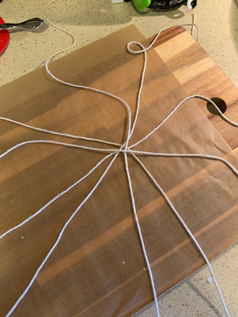 Five lengths of twine, all crossing at the center, on a piece of parchment paper on a wooden cutting board.