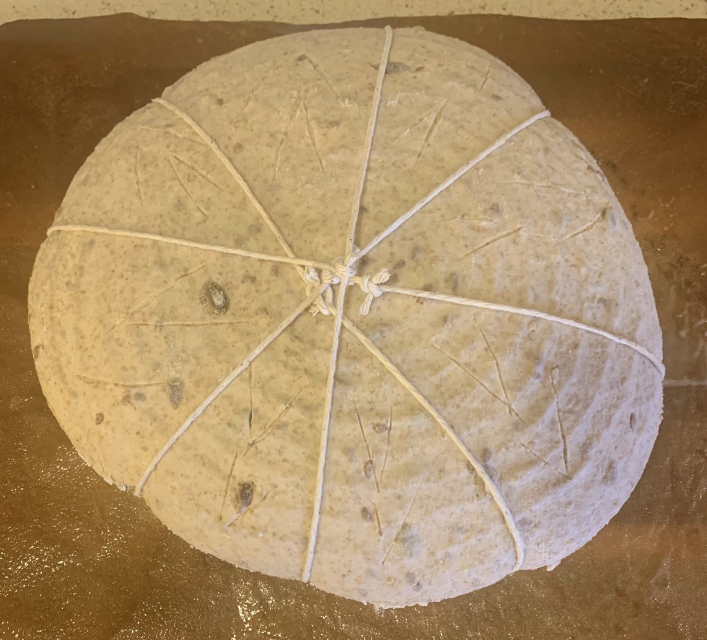 Dough about to bake, tied with four strings and scored with v shapes between the strings.
