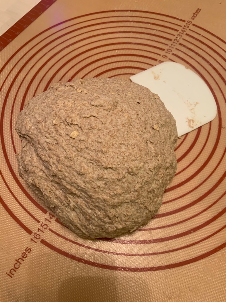 Kneaded ball of grainy dough on a rubber mat next to a bench scraper.