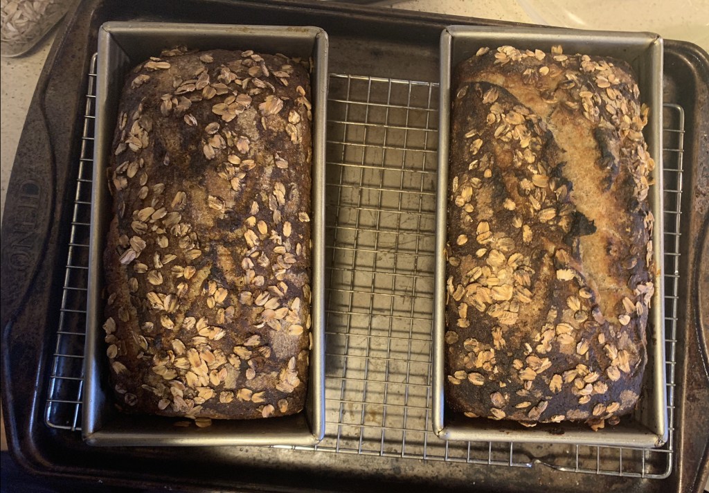 Two loaves of baked bread, still in tins, on a wire rack on a baking tray.